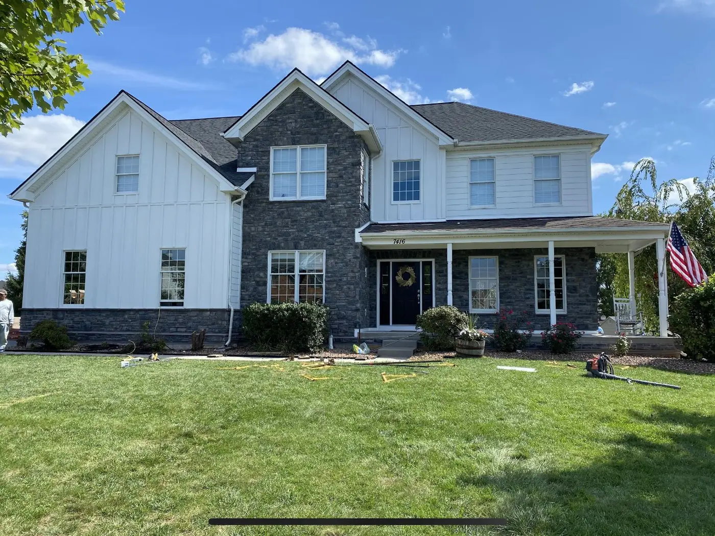 Two-story home with white board-and-batten siding, stone front and a shingle roof